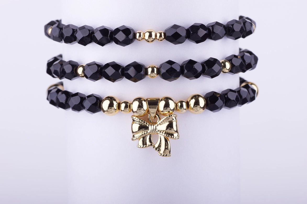 Set de 3 Pulseras de Cuentas de Cristal Negro Azabache y charm de Lazo en Oro Laminado. Elegancia atemporal y envío rápido.