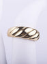 Anillo ancho dorado con textura de líneas diagonales en relieve tipo croissant sobre fondo blanco.