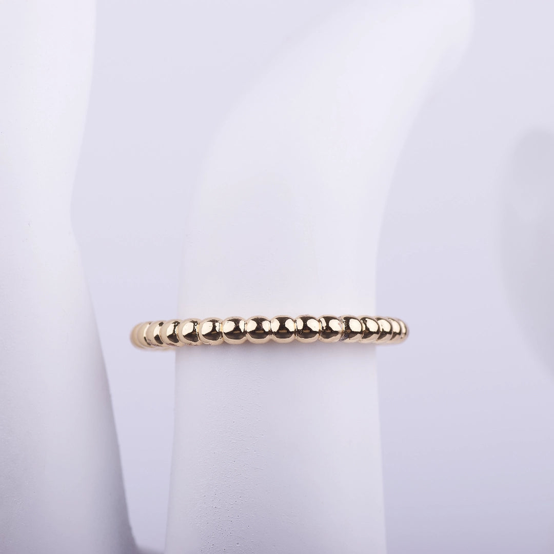 Anillo delgado dorado con textura de pequeñas esferas continuas sobre fondo blanco, estilo minimalista.