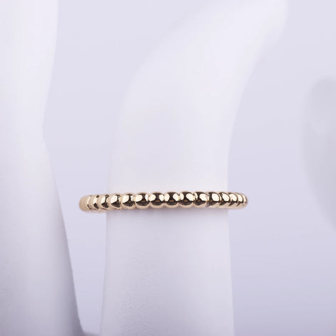 Anillo delgado dorado con textura de pequeñas esferas continuas sobre fondo blanco, estilo minimalista.