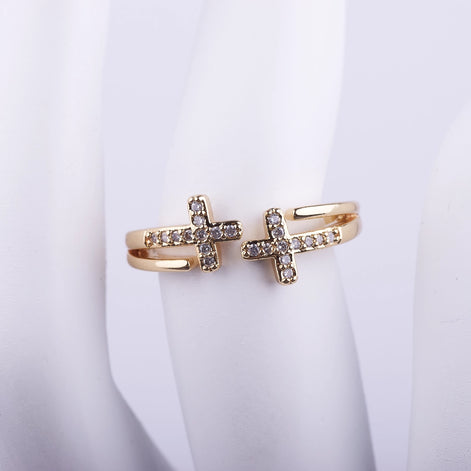 Anillo abierto dorado de doble banda con dos cruces frontales decoradas con cristales brillantes sobre fondo blanco.