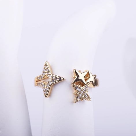 Anillo abierto dorado con diseño de estrellas asimétricas, una de ellas con cristales brillantes pavé sobre fondo blanco.