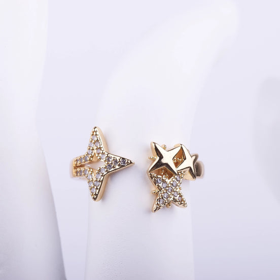 Anillo abierto dorado con diseño de estrellas asimétricas, una de ellas con cristales brillantes pavé sobre fondo blanco.