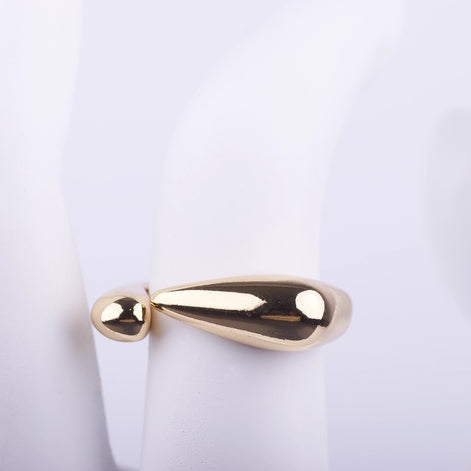 Anillo abierto dorado con extremos en forma de gota fluida y acabado brillante sobre fondo blanco.