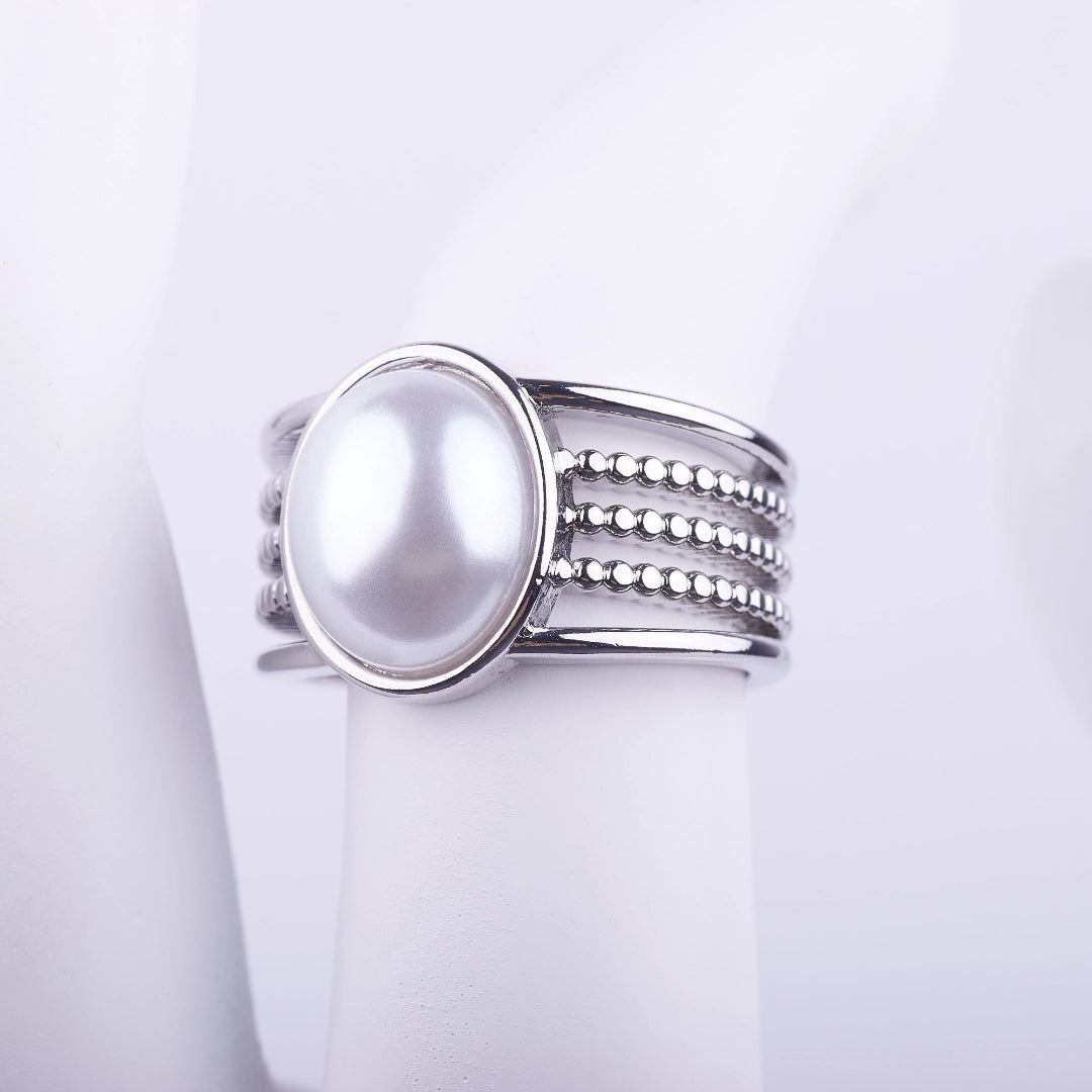 Anillo ancho plateado con una gran perla central y banda decorativa de cinco niveles lisos y de cuentas sobre fondo blanco.