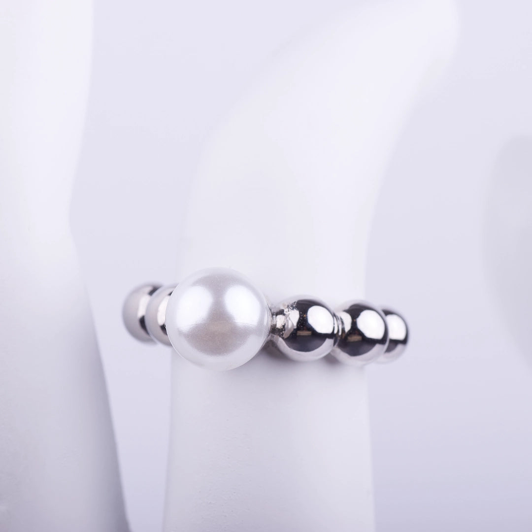 Anillo plateado con una perla blanca central y banda compuesta por pequeñas esferas brillantes sobre fondo blanco.