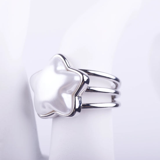 Anillo plateado de tres bandas con una gran perla central en forma de estrella sobre fondo blanco.