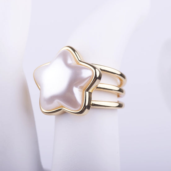 Anillo de tres bandas doradas con una gran perla central en forma de estrella blanca sobre fondo blanco.