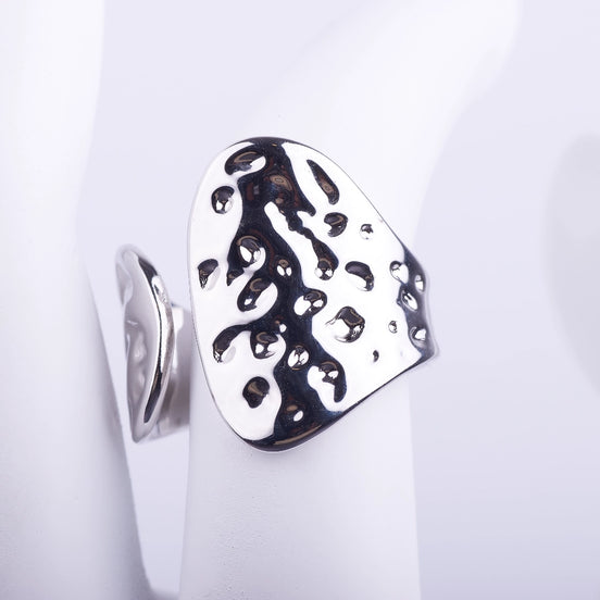 Anillo ajustable ancho de acabado plateado con textura de hoyuelos irregulares y brillo espejo sobre fondo blanco.