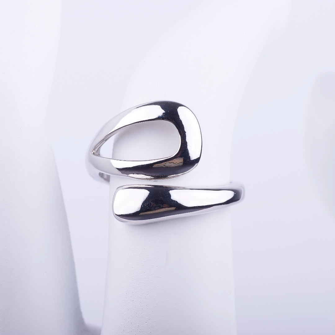 Anillo abierto plateado de diseño fluido con forma de gota estilizada y acabado brillante sobre fondo blanco.