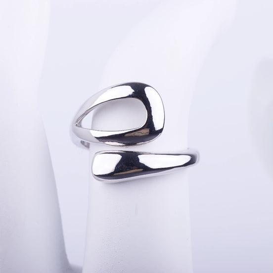 Anillo abierto plateado de diseño fluido con forma de gota estilizada y acabado brillante sobre fondo blanco.