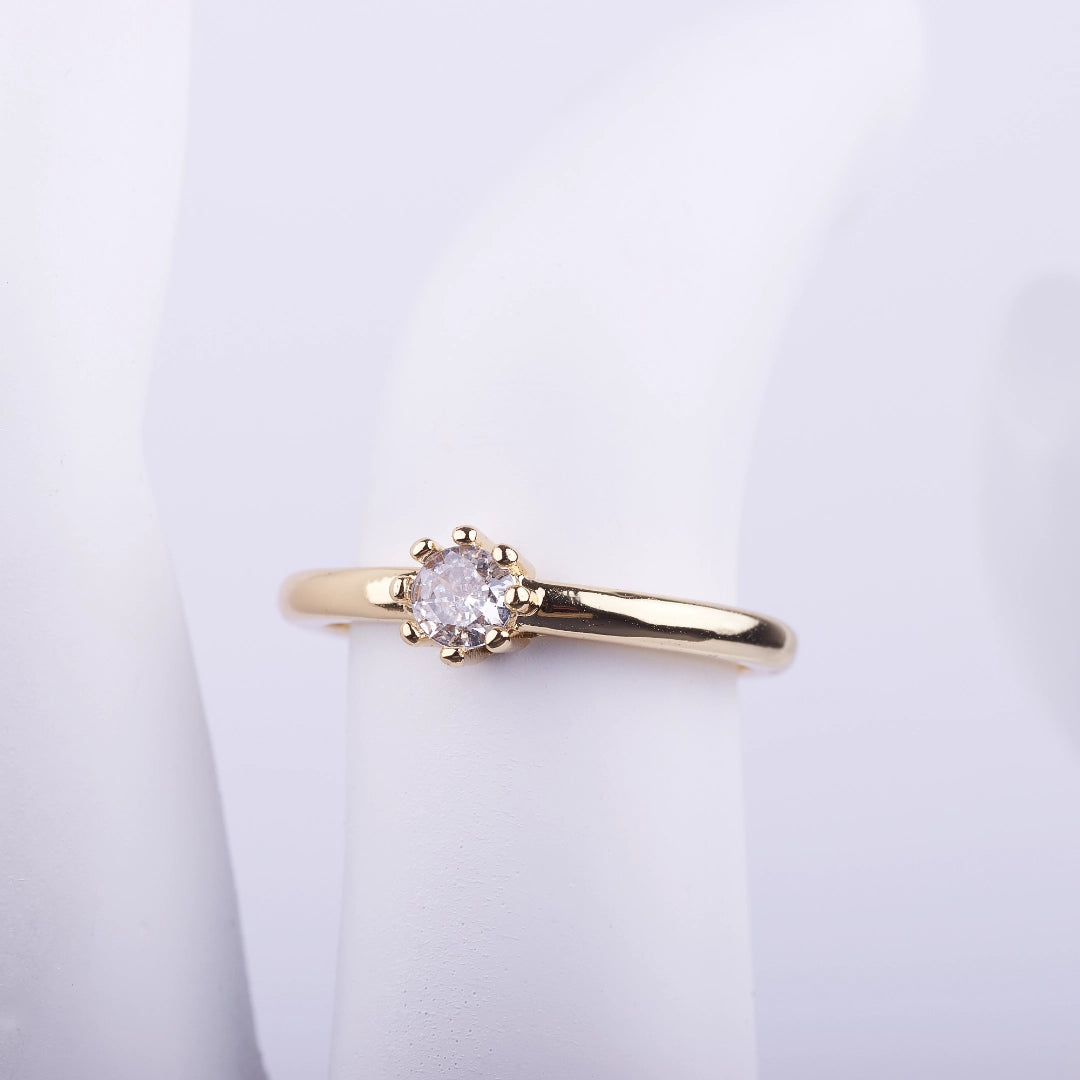Anillo delgado con acabado dorado y piedra central brillante sobre soporte blanco, estilo minimalista de moda.