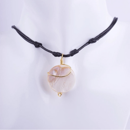 Collar estilo choker de cordón de macramé negro con un dije de nácar natural redondo envuelto en alambre dorado. El cordón tiene nudos corredizos, exhibido en un busto de maniquí gris oscuro.