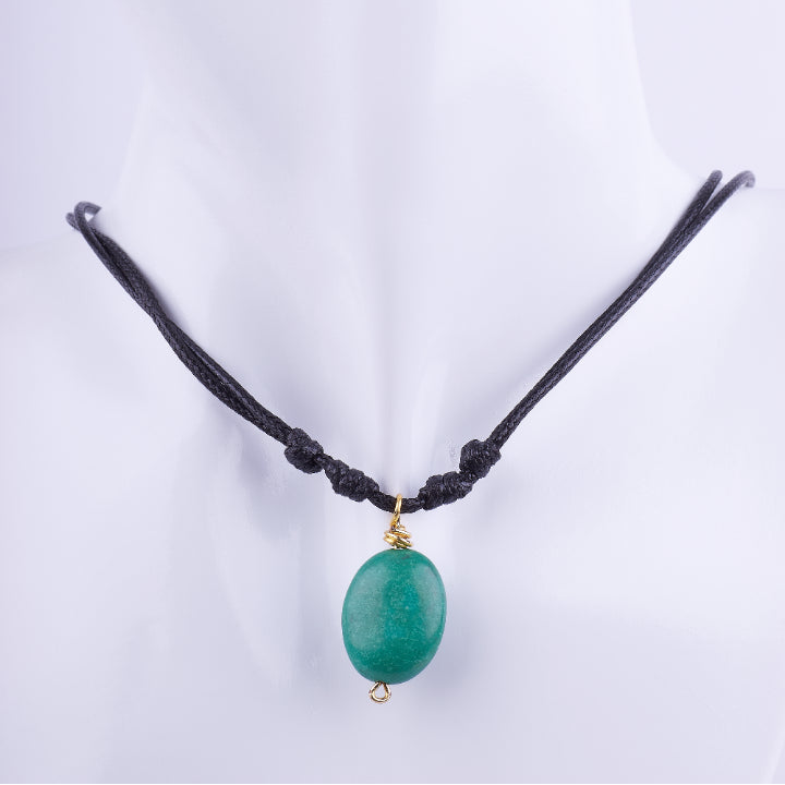Collar estilo choker de cordón doble de macramé negro con un dije de piedra natural ovalada de color verde jade. La piedra está envuelta en alambre dorado, exhibido en un busto de maniquí blanco.