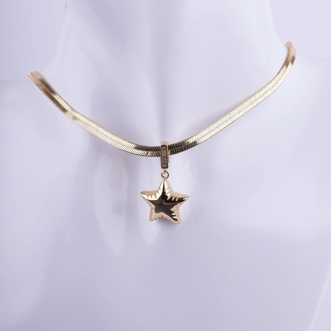 Collar de cadena plana tipo serpiente (herringbone) bañada en oro, con dije de estrella voluminosa y detalles de zirconia. Joyería de alta moda.