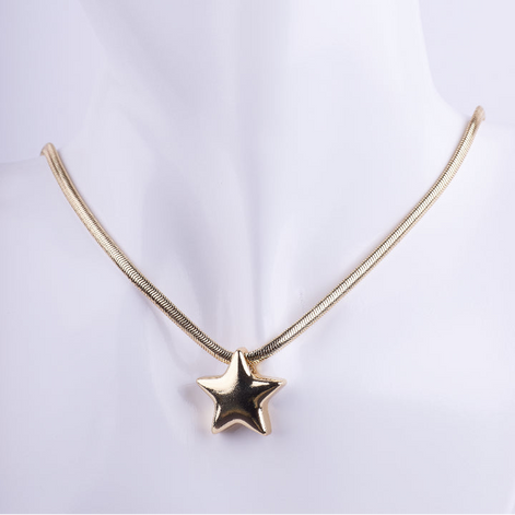 Collar estilo choker de cadena serpiente (snake chain) dorada con un dije de estrella voluminoso (puffy) y liso. El dije tiene un acabado de metal espejo brillante, exhibido en un busto de maniquí blanco.