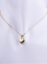 Collar de cadena de eslabones dorados finos con un dije de corazón inflado (puffy) de metal liso y muy pulido. El corazón es de color dorado y está exhibido en un busto de maniquí blanco.