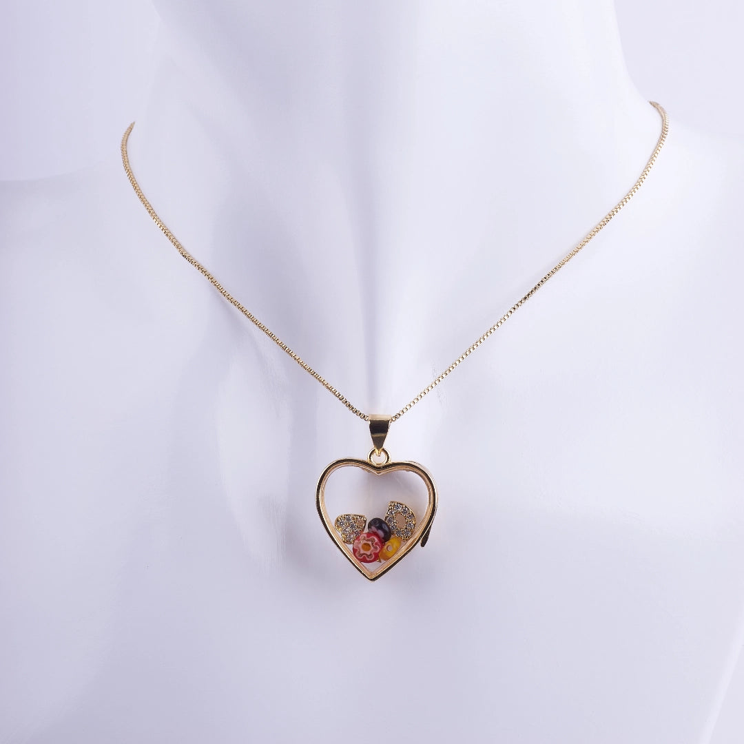Collar de corazón tipo relicario flotante con marco bañado en oro, flores minúsculas encapsuladas, y detalles de zirconias. Joyería romántica para regalo.