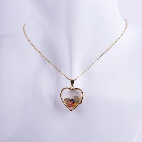 Collar de corazón tipo relicario flotante con marco bañado en oro, flores minúsculas encapsuladas, y detalles de zirconias. Joyería romántica para regalo.