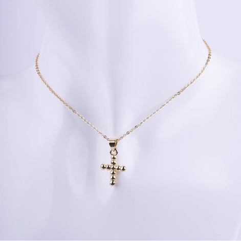 Collar de cadena de eslabones finos dorados con un dije de cruz tridimensional formado por pequeñas esferas doradas en relieve. Exhibido en un busto de maniquí blanco.