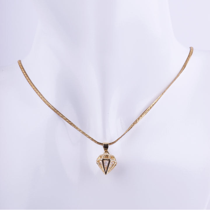 Collar de cadenilla dorada tipo serpiente con un dije colgante en forma geométrica y facetada de un diamante. El dije es de metal liso y brillante, exhibido en un busto de maniquí blanco.