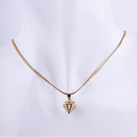 Collar de cadenilla dorada tipo serpiente con un dije colgante en forma geométrica y facetada de un diamante. El dije es de metal liso y brillante, exhibido en un busto de maniquí blanco.