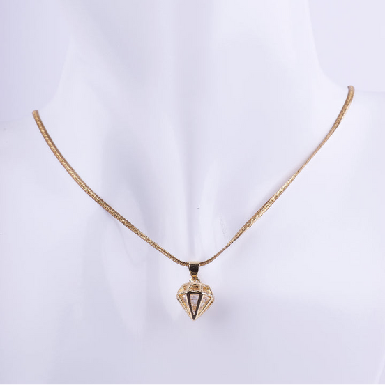 Collar de cadenilla dorada tipo serpiente con un dije colgante en forma geométrica y facetada de un diamante. El dije es de metal liso y brillante, exhibido en un busto de maniquí blanco.