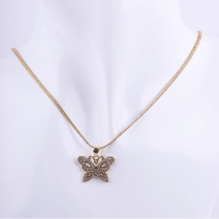 Collar de cadenilla dorada tipo serpiente con dije de mariposa calada. El dije está decorado con micro-engaste de piedras brillantes en las alas, exhibido en un busto de maniquí blanco.