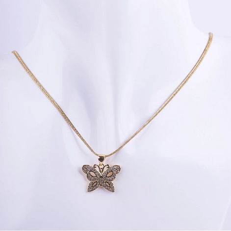 Collar de cadenilla dorada tipo serpiente con dije de mariposa calada. El dije está decorado con micro-engaste de piedras brillantes en las alas, exhibido en un busto de maniquí blanco.