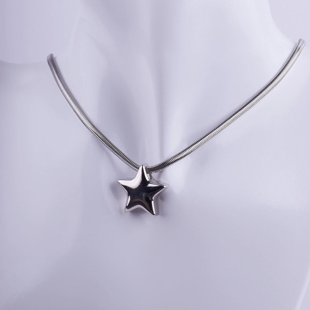 Collar plateado con dije de estrella en 3D y cadena tipo serpiente sobre maniquí blanco, joyería de acero inoxidable estilo moderno.