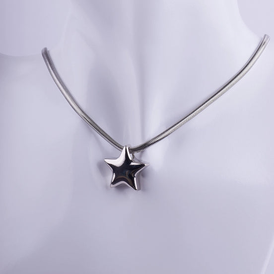Collar plateado con dije de estrella en 3D y cadena tipo serpiente sobre maniquí blanco, joyería de acero inoxidable estilo moderno.