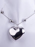Collar gargantilla con dije de corazón maxigrueso plateado y pulido, montado sobre cadena tipo serpiente con esferas metálicas.