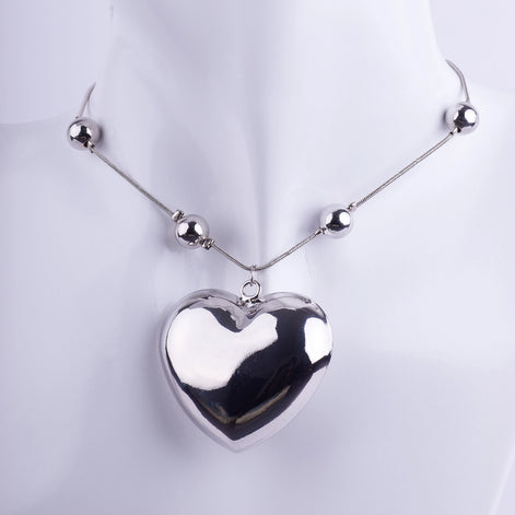 Collar gargantilla con dije de corazón maxigrueso plateado y pulido, montado sobre cadena tipo serpiente con esferas metálicas.