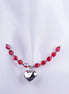 Collar gargantilla con cuentas de cristal rojo facetado y dije de corazón plateado pulido en maniquí blanco. Joyería romántica y de fiesta.