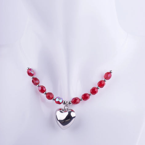 Collar gargantilla con cuentas de cristal rojo facetado y dije de corazón plateado pulido en maniquí blanco. Joyería romántica y de fiesta.