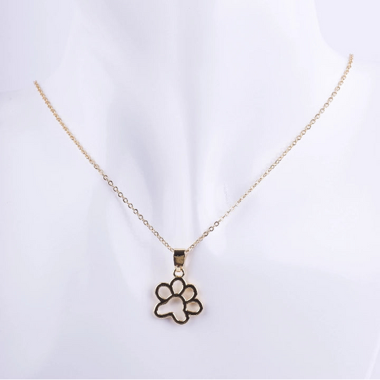 Collar de cadena de eslabones dorados finos con un dije colgante de huella de pata de animal con diseño calado. El dije es de metal liso y brillante, exhibido en un busto de maniquí blanco.