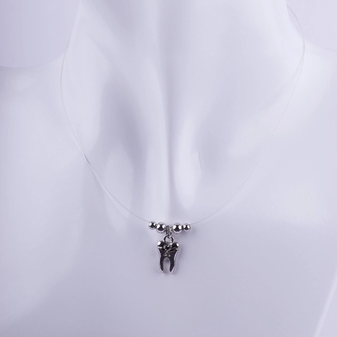 Collar de hilo invisible con dije de muela plateada y pequeñas esferas de metal, joyería temática para profesionales de la odontología.