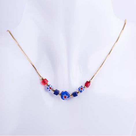 Collar de cadenilla dorada con nueve cuentas de cristal de Murano de colores rojo y azul, exhibido en un busto blanco. El detalle central es una cuenta azul con diseño de flor roja y blanca.