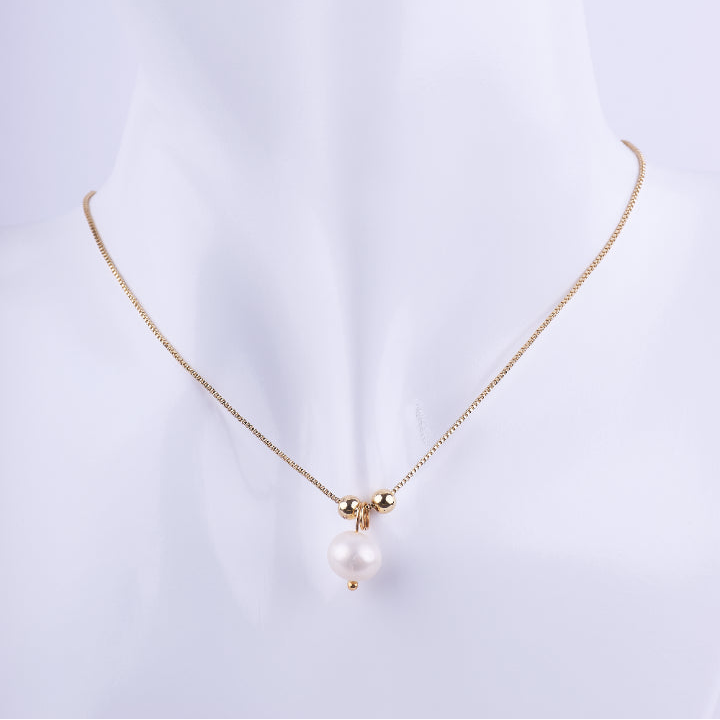 Collar de cadena tipo veneciana dorada con un dije colgante de perla blanca, flanqueada por dos pequeñas esferas doradas. Exhibido en un busto de maniquí blanco