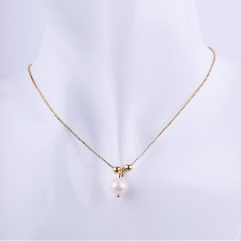 Collar de cadena tipo veneciana dorada con un dije colgante de perla blanca, flanqueada por dos pequeñas esferas doradas. Exhibido en un busto de maniquí blanco