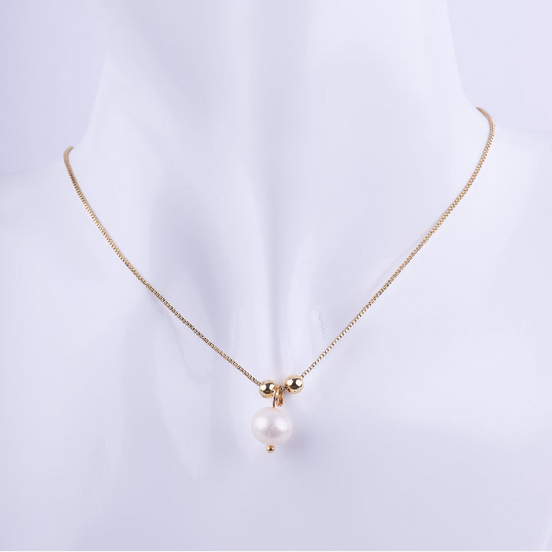 Collar de cadena tipo veneciana dorada con un dije colgante de perla blanca, flanqueada por dos pequeñas esferas doradas. Exhibido en un busto de maniquí blanco