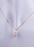 Collar dorado con dos perlas naturales colgando verticalmente, una blanca y una rosa, sobre una cadena veneciana fina.