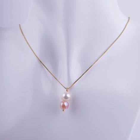 Collar dorado con dos perlas naturales colgando verticalmente, una blanca y una rosa, sobre una cadena veneciana fina.