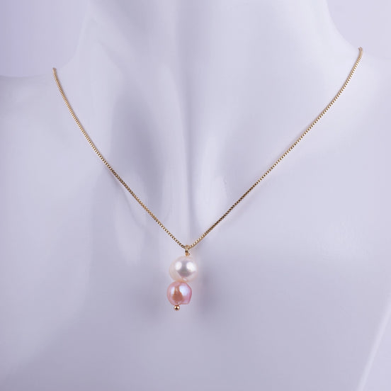 Collar dorado con dos perlas naturales colgando verticalmente, una blanca y una rosa, sobre una cadena veneciana fina.