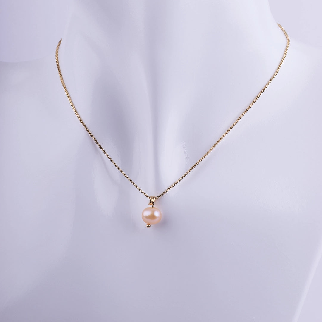 Collar minimalista con una perla natural color melocotón colgando de una cadena veneciana bañada en oro sobre un busto de exhibición.