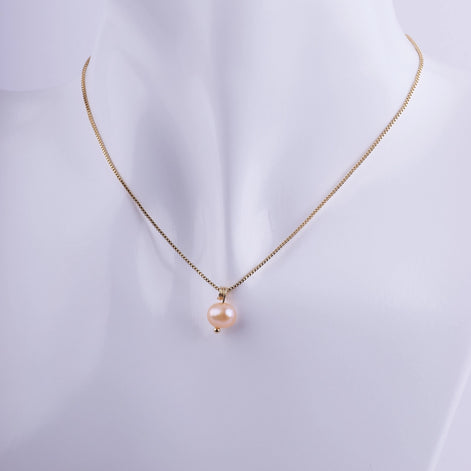 Collar minimalista con una perla natural color melocotón colgando de una cadena veneciana bañada en oro sobre un busto de exhibición.