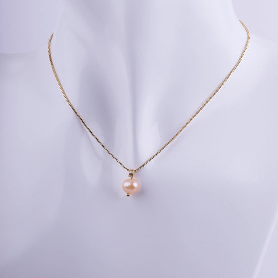 Collar minimalista con una perla natural color melocotón colgando de una cadena veneciana bañada en oro sobre un busto de exhibición.