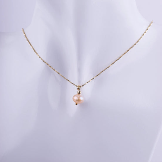 Collar de cadena veneciana dorada con colgante de perla natural color melocotón sobre busto blanco, joyería elegante de estilo minimalista.