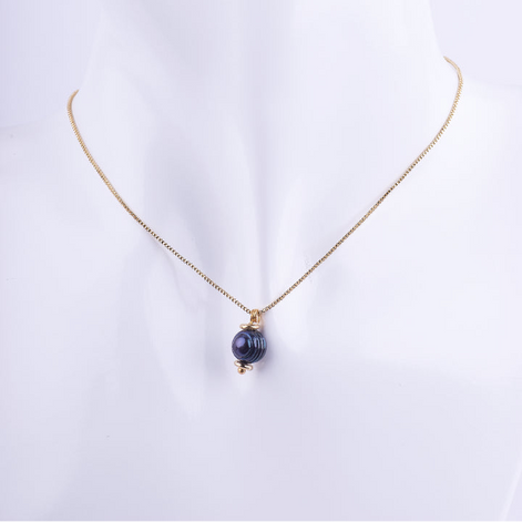 Collar de cadena tipo veneciana dorada con un dije de una perla negra redonda. La perla está coronada por una pequeña cuenta dorada, exhibida en un busto de maniquí blanco.