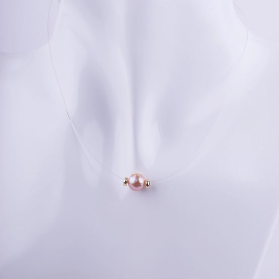 Gargantilla de hilo invisible con una perla rosa natural y dos pequeñas cuentas doradas a los lados, estilo flotante minimalista.